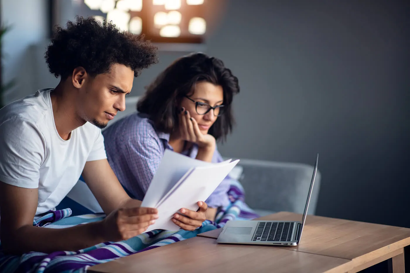 Concerned young couple looking at the papers while using the laptop in the living room