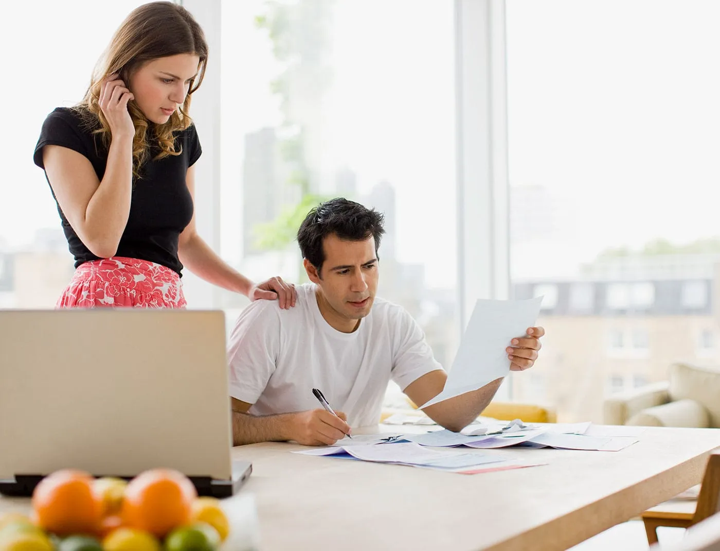 A couple frown together as they look at a document on their kitchen table.