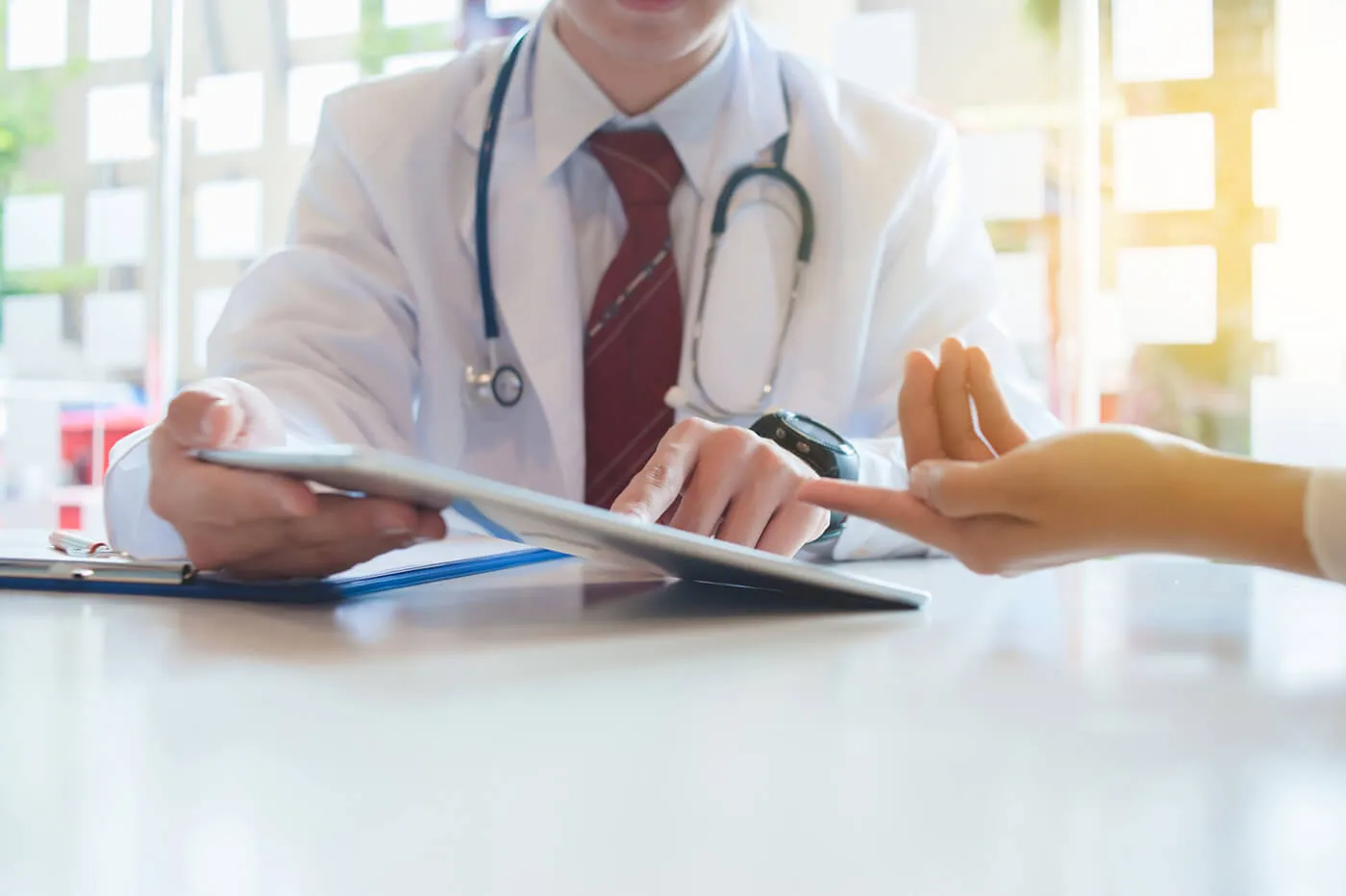 male doctor with stethoscope around neck holding a keyboard while seated and pointing at it