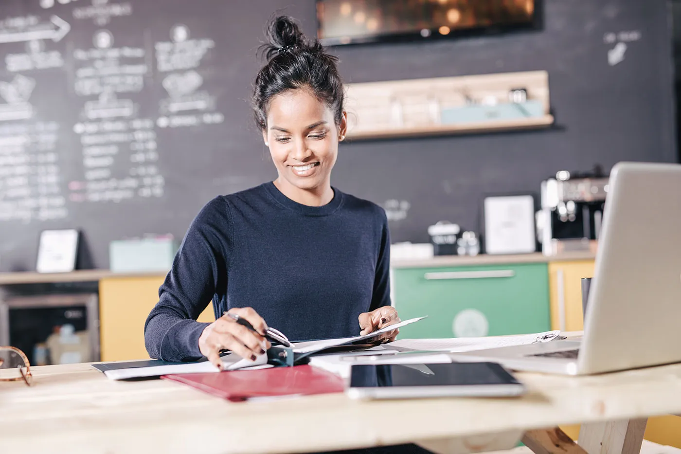 A woman wearing a black shirt smiles as she looks over a folder with documents with a laptop next to her.