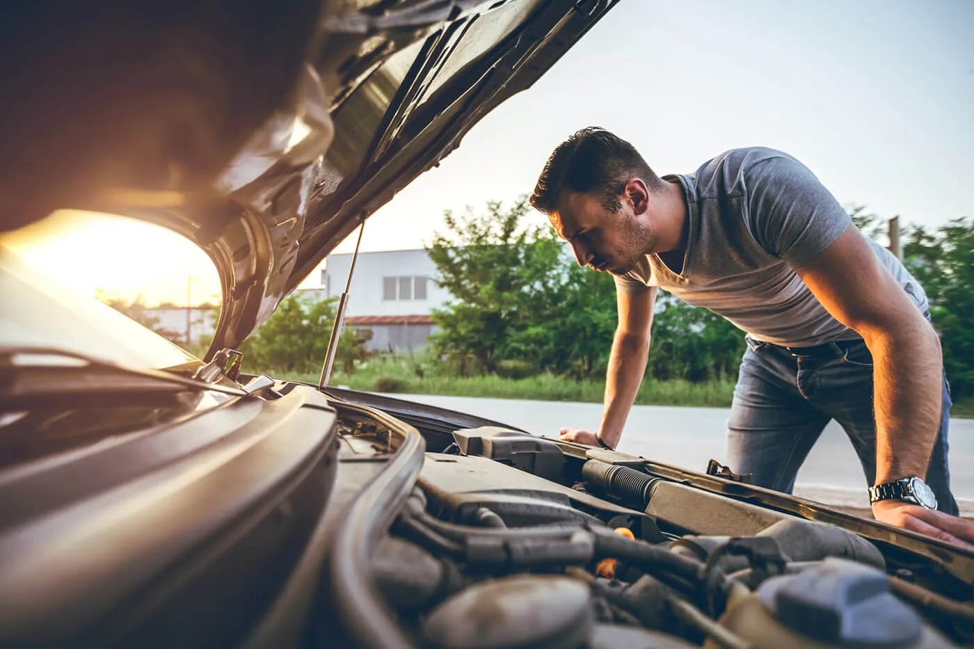 Young man is standing next to a broken down car, examining under the hood