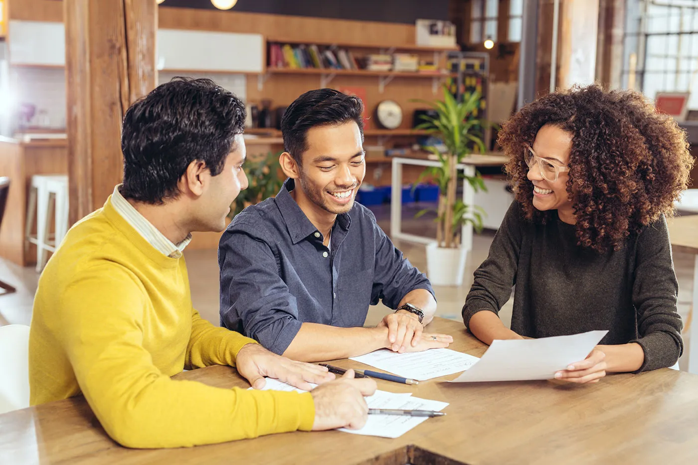 A group of three people smile and laugh with each other while looking at a document.