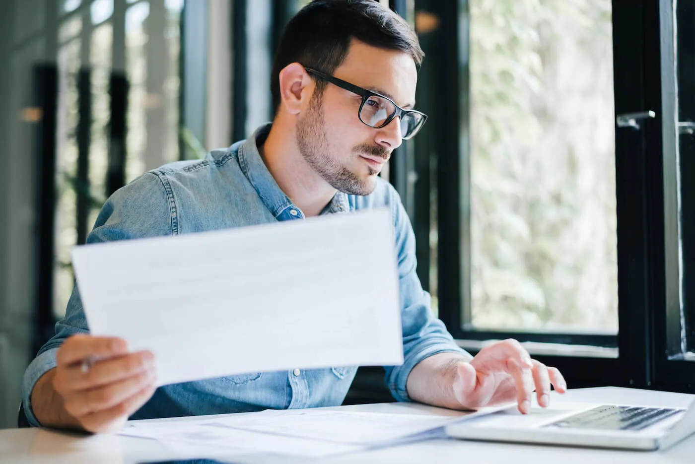 man holding paper while typing on laptop on a desk