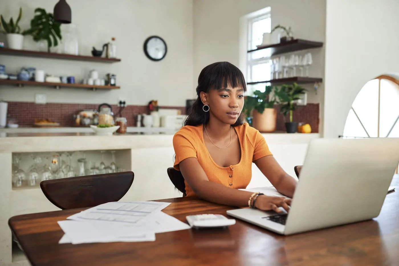 woman in orange t-shirt seated at a table researching on a laptop how to cancel a pending transaction