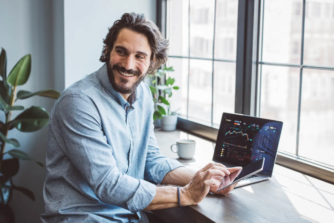 smiling man seated at a desk by an open laptop