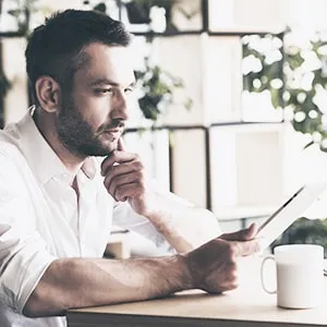 man in white shirt holding a paper and looking in thought