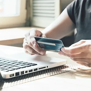 A person holding a credit card in front of a laptop.