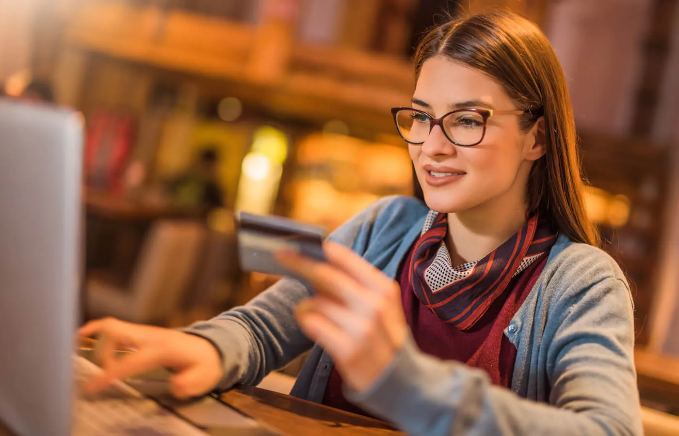 A woman wearing a red shirt uses her laptop while holding her credit card.