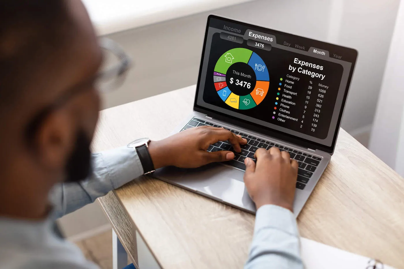 A man looks at a pie graph of his expenses by category on his laptop computer screen.