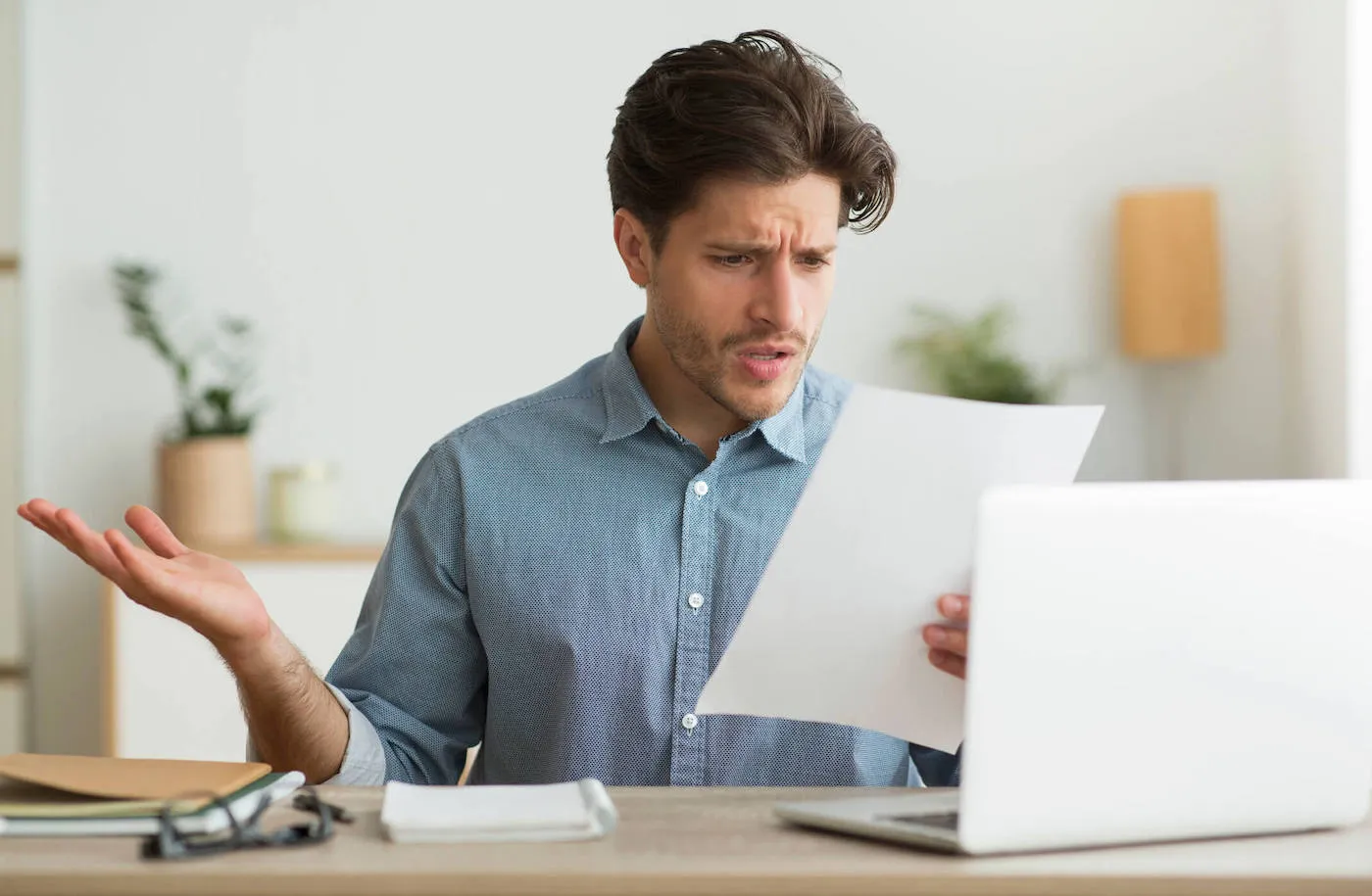 A man wearing a blue shirt has a surprised look on his face as he looks at a document.