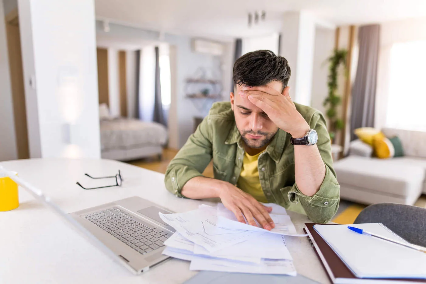 A man frowns while he has his hand to his forehead while looking at documents on the table.