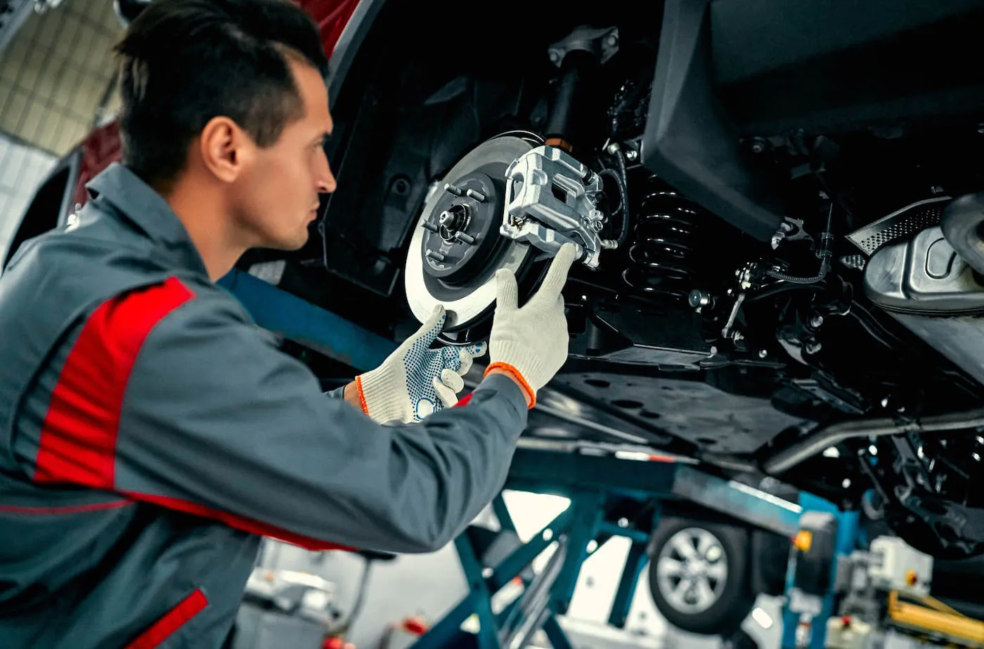 A mechanic wearing his uniform works on a wheel rotor of a car at the factory.