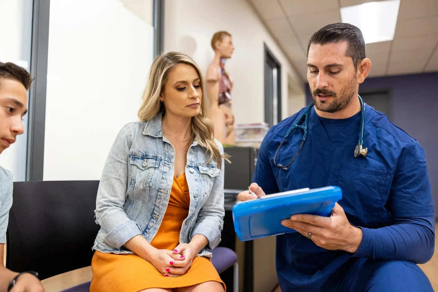 A Nurse receptionist explains a medical bill to a woman with her son at the doctors office waiting room lobby.