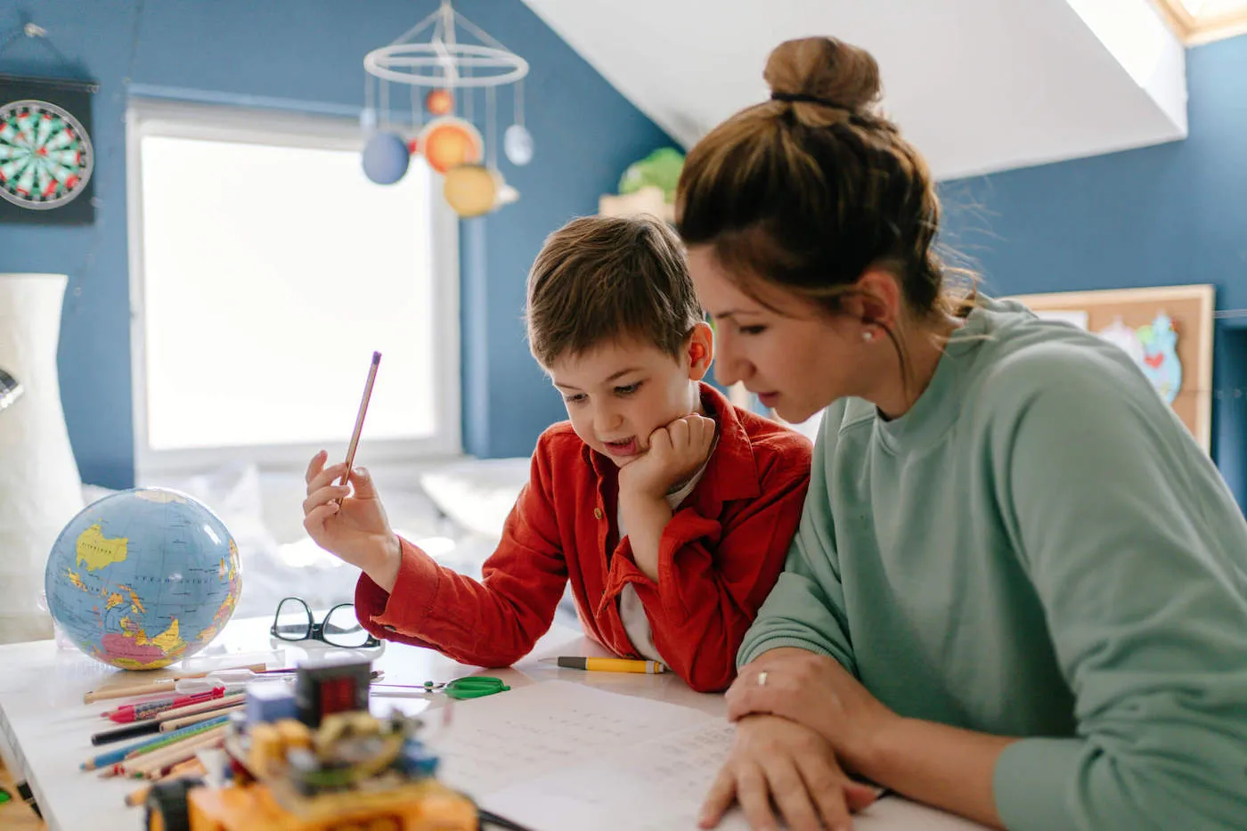 A mom helps her son with homework while inside of his bedroom.