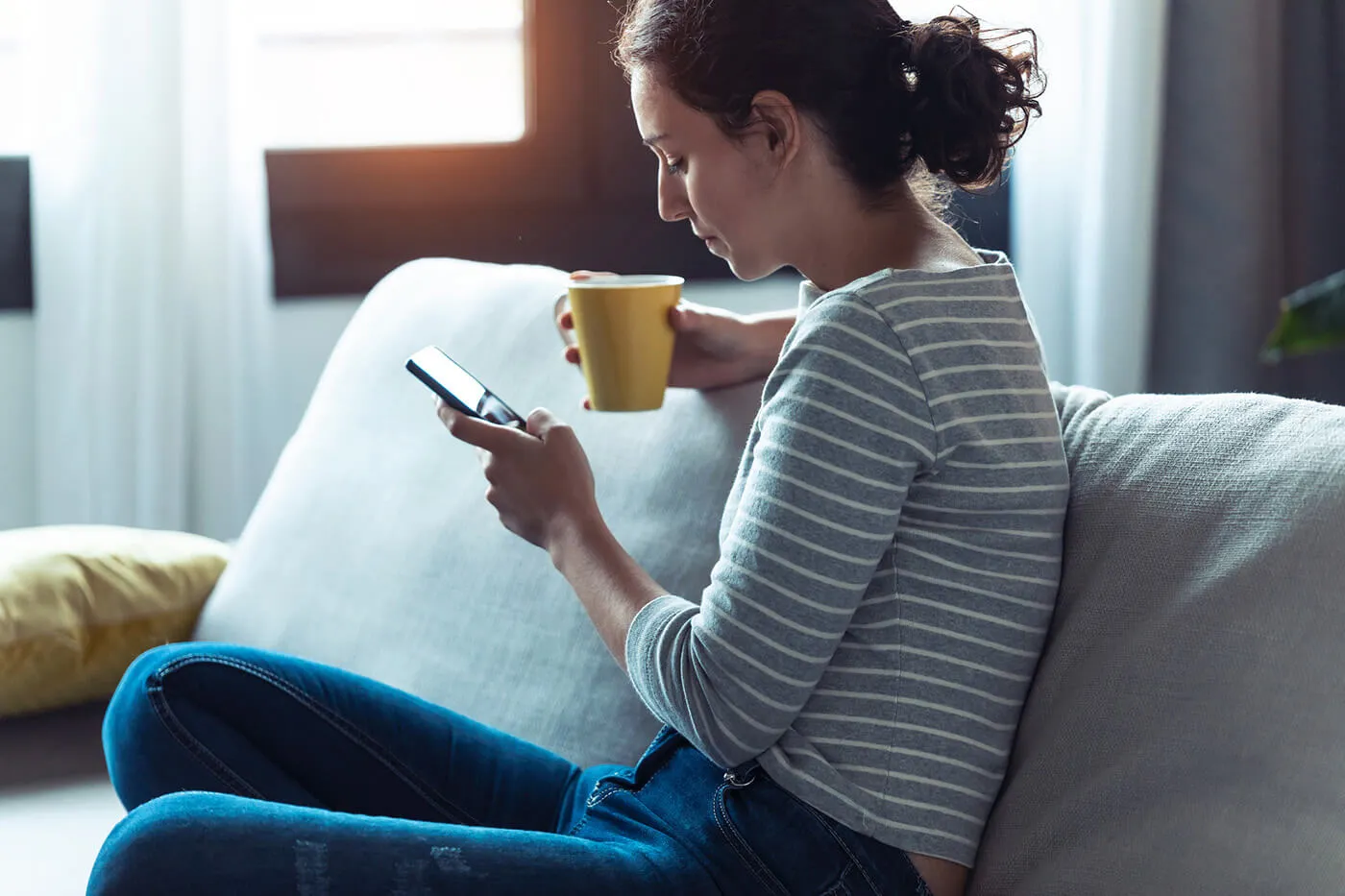 Serious young woman using her mobile phone while sitting on sofa in the living room at home.