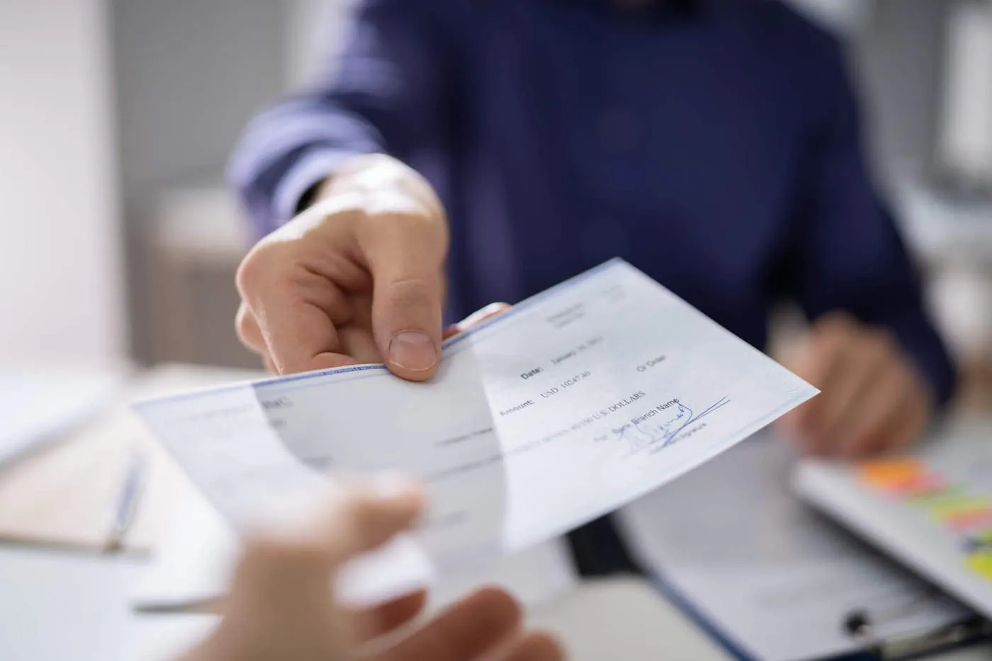 A person wearing a blue sweater hands a check to another table from across the table.