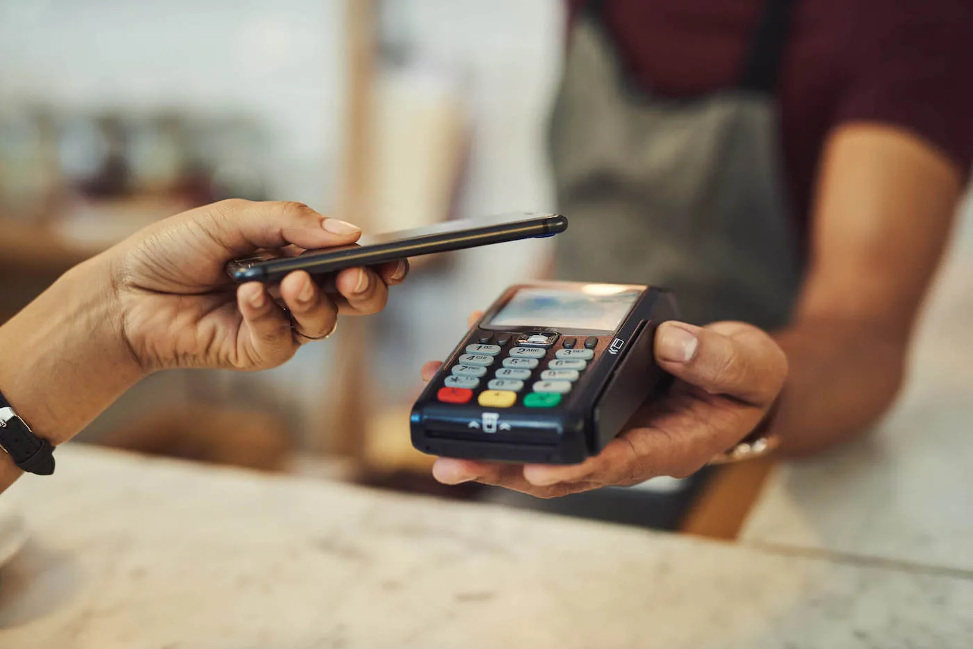 A person hold up their phone to a card reader to pay.