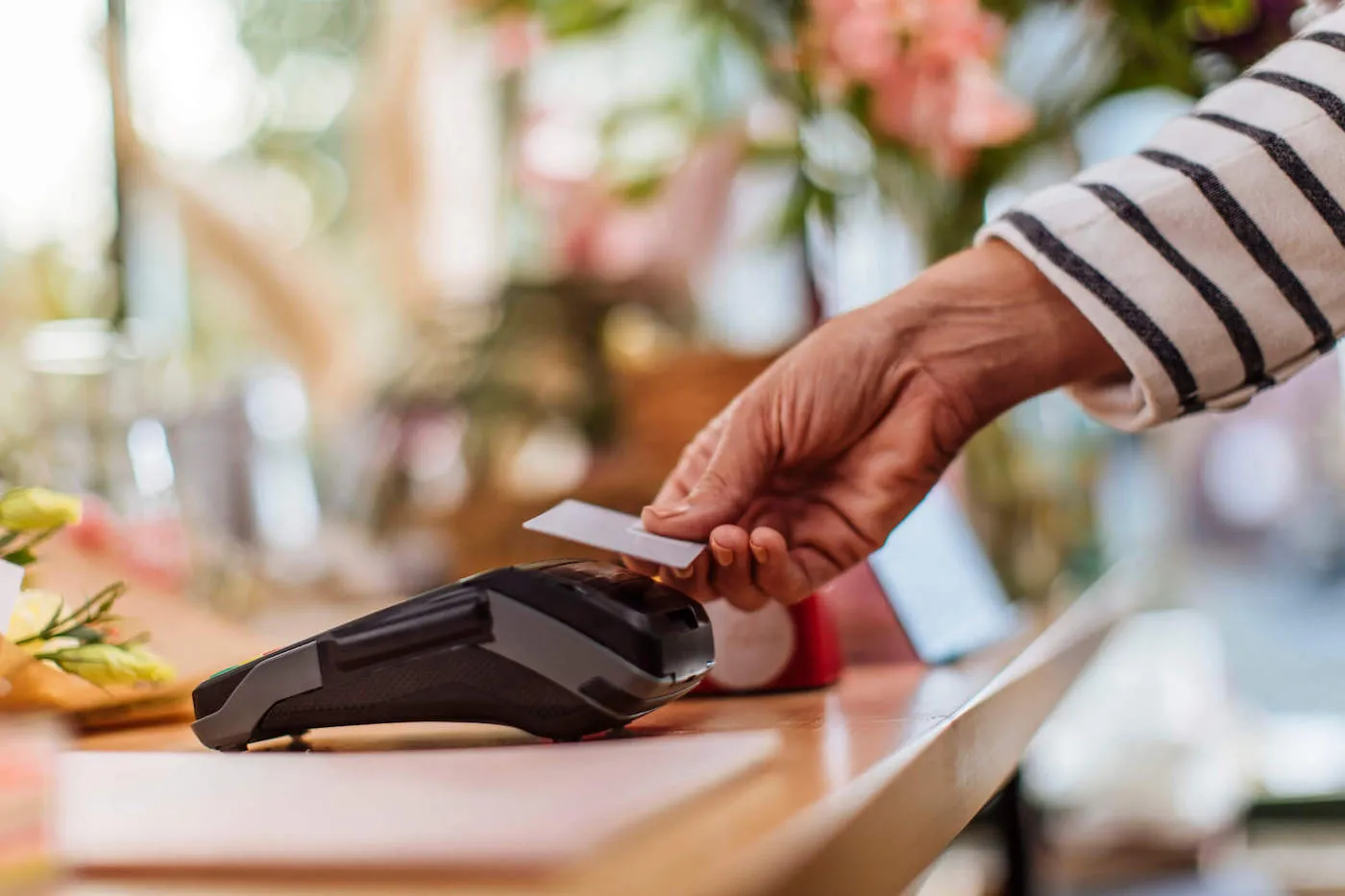 A person wearing a striped shirt taps their credit card on the credit card reader to pay.