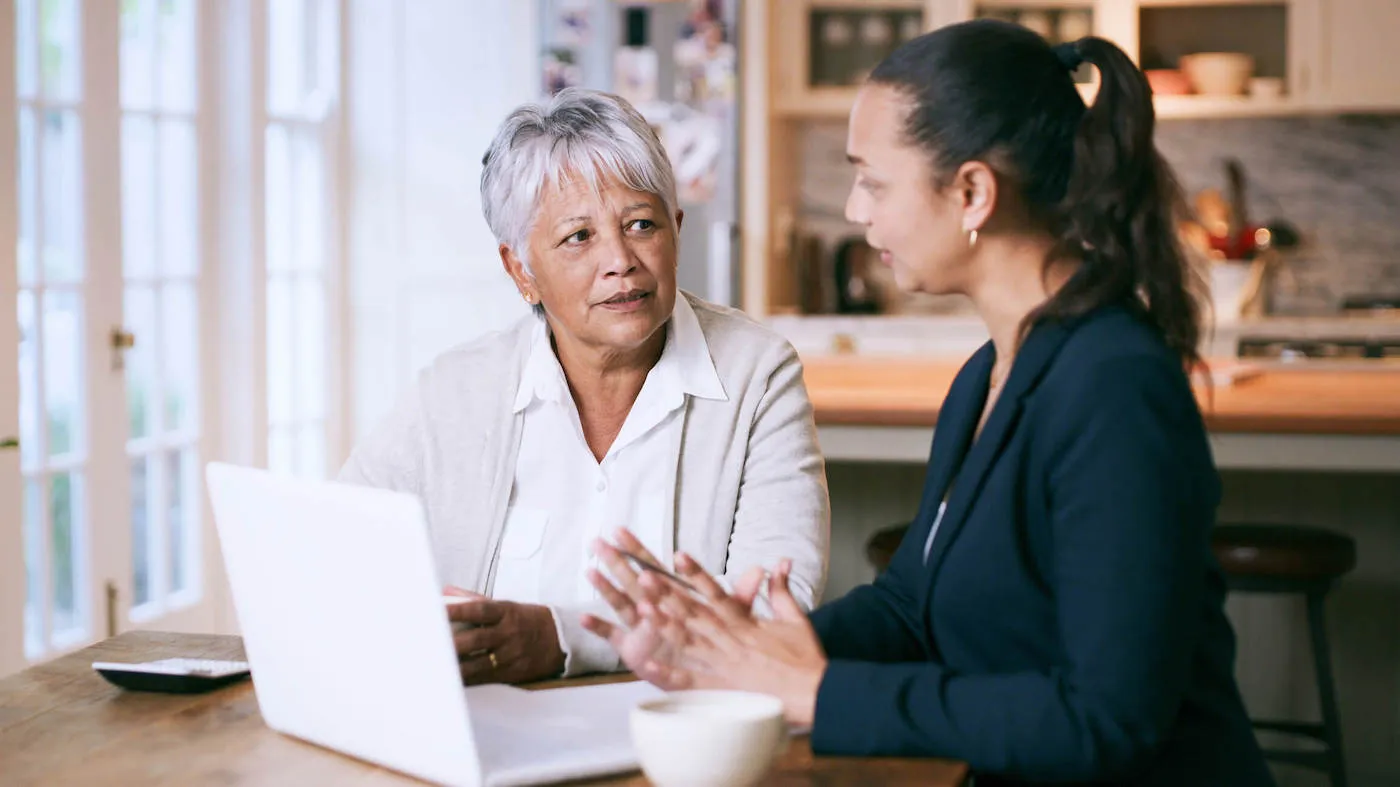 Shot of a senior woman using a laptop during a meeting with a consultant at home.