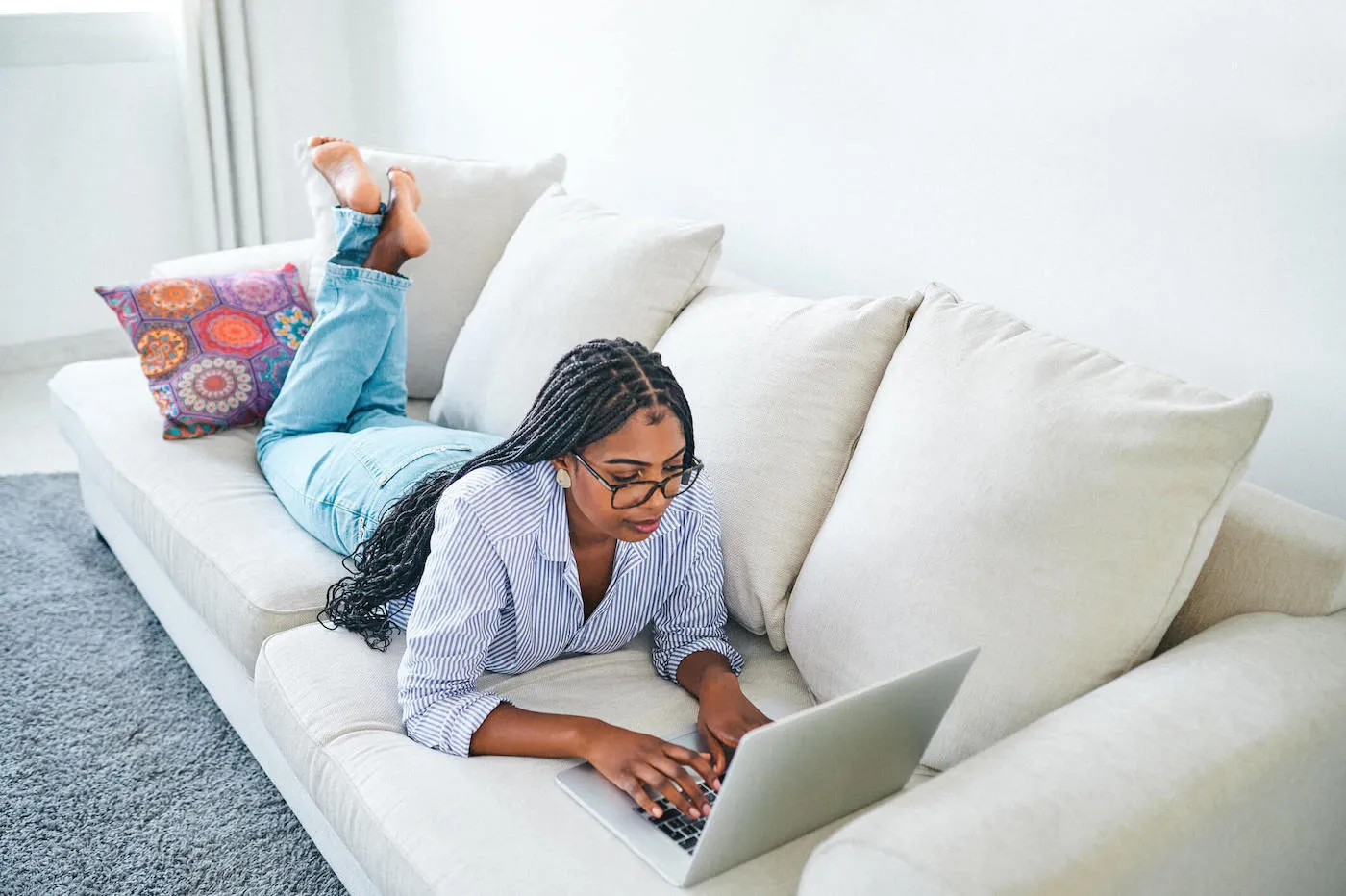 Shot of a young female using the laptop while laying on the couch at home.