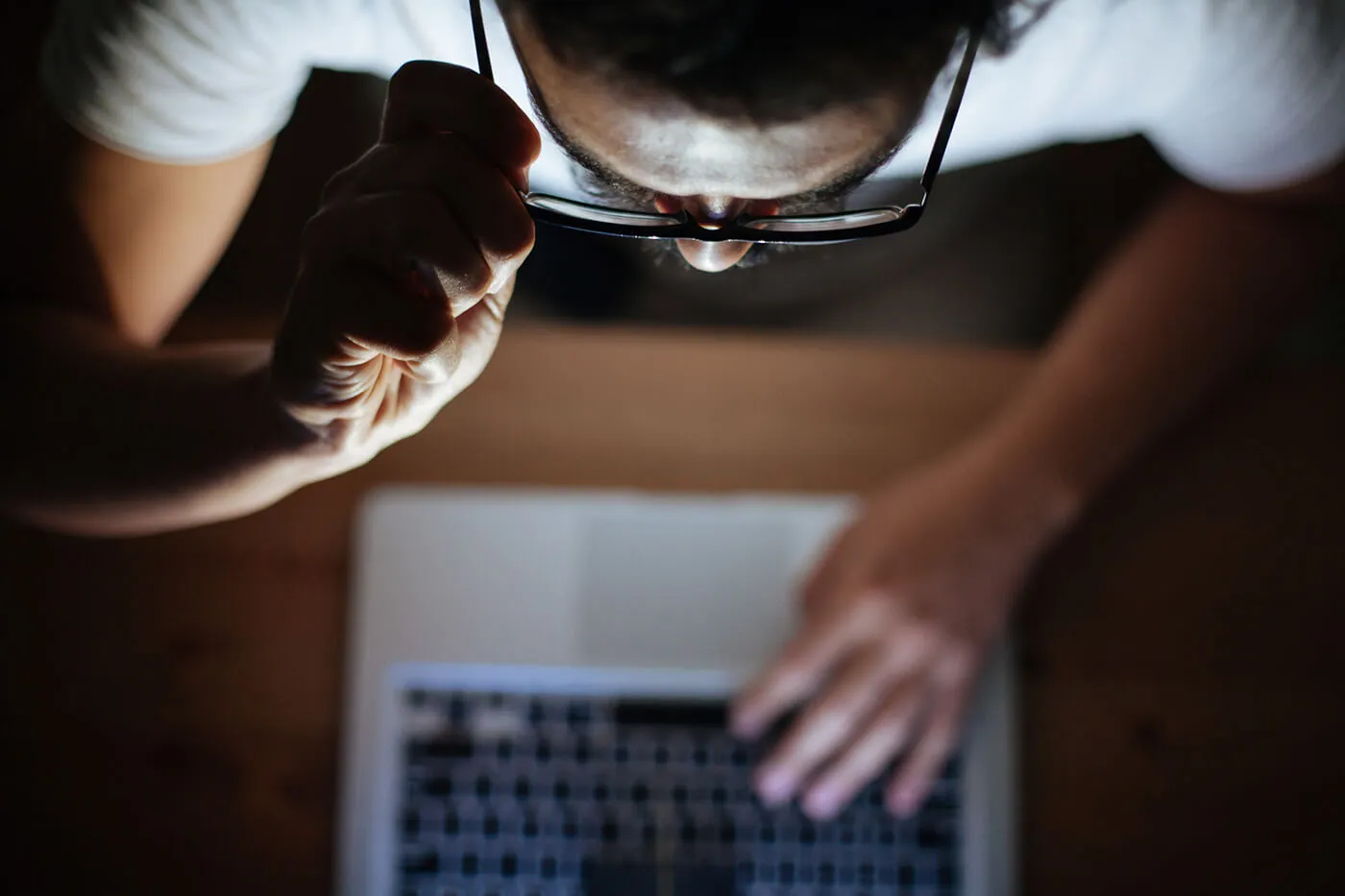 man with glasses and white t-shirt looking at laptop