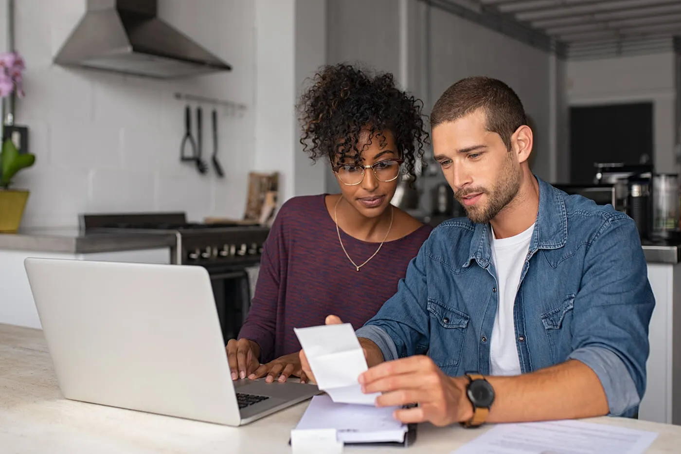 A young couple checking their bills and using a laptop in the kitchen