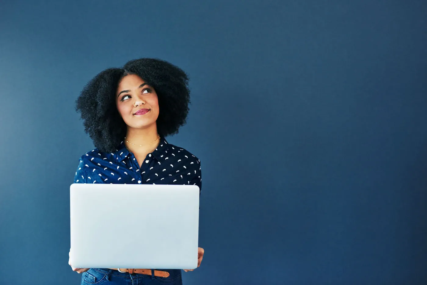 A young woman looking up while using a laptop against a blue background.