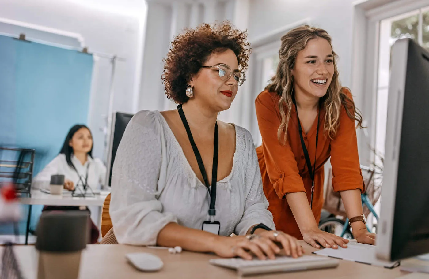 A pair of coworkers smile at a computer screen while working at the office.