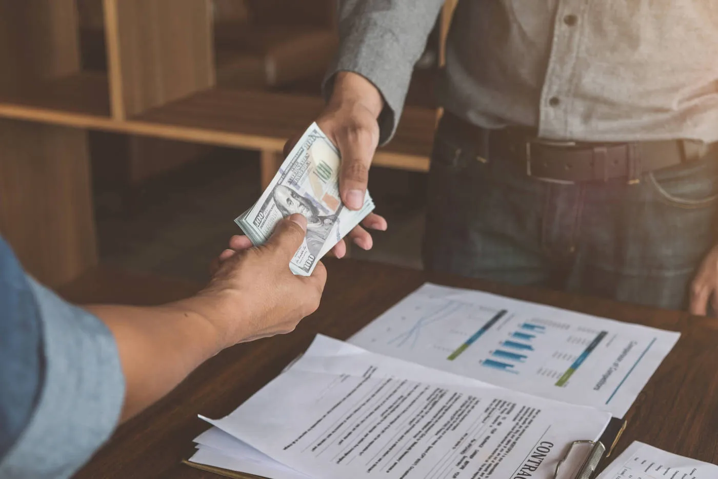 A person hands another person money while a contract sits on the table.