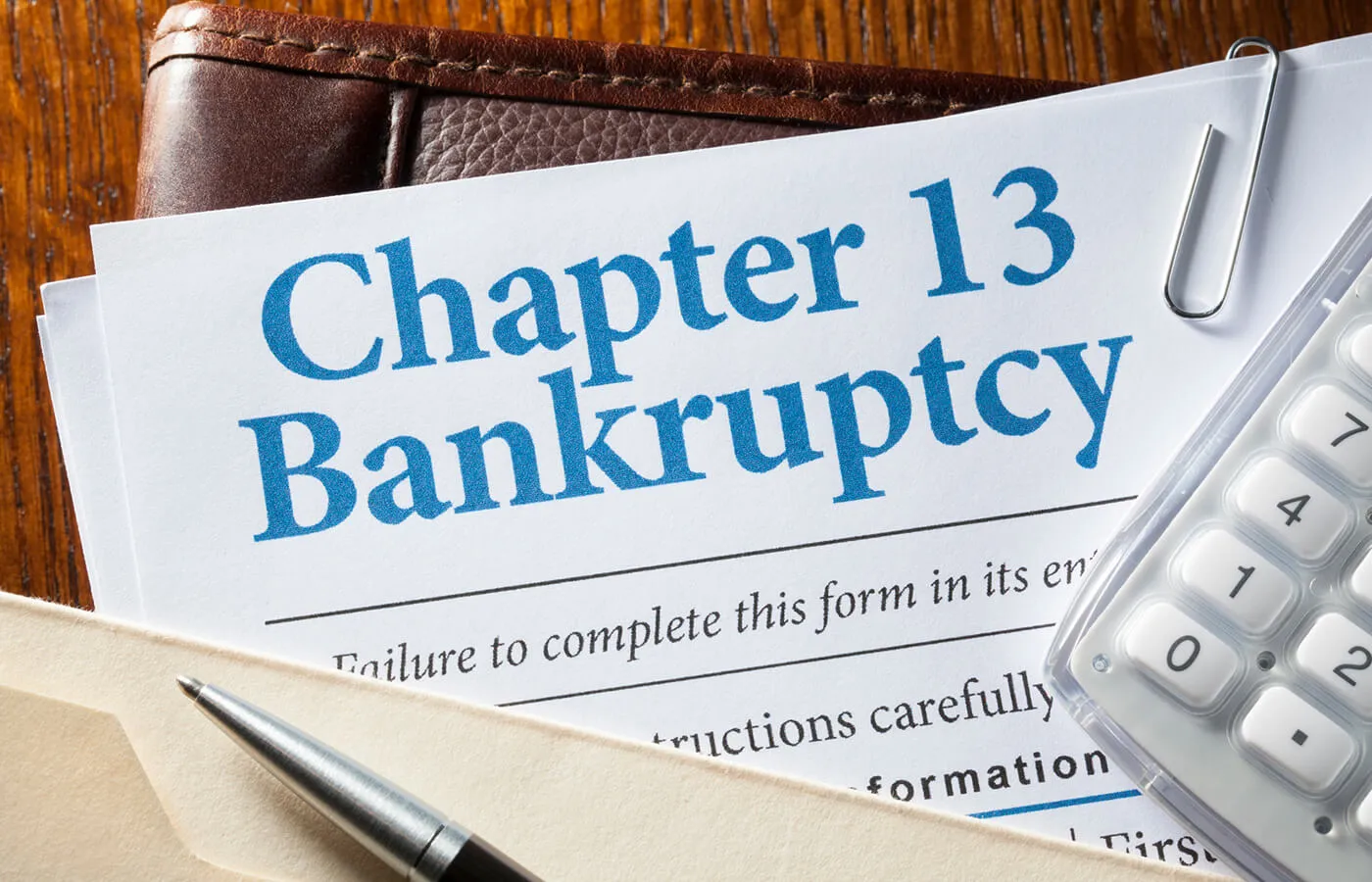 A stack of papers titled "Chapter 13 Bankruptcy" sitting on top of a folder a desk with a calculator on top.