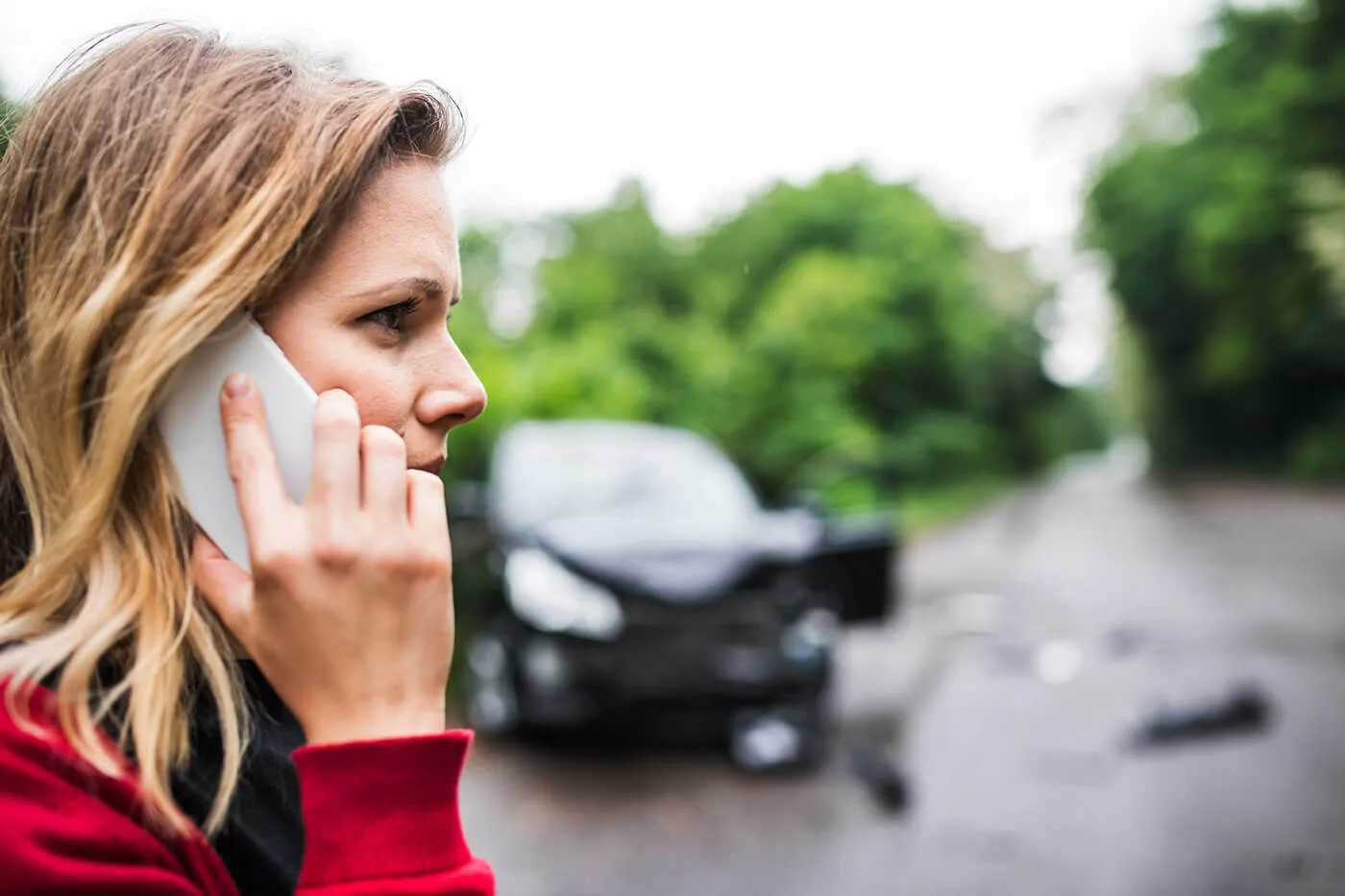 A young woman on the phone standing by the damaged car after a car accident.