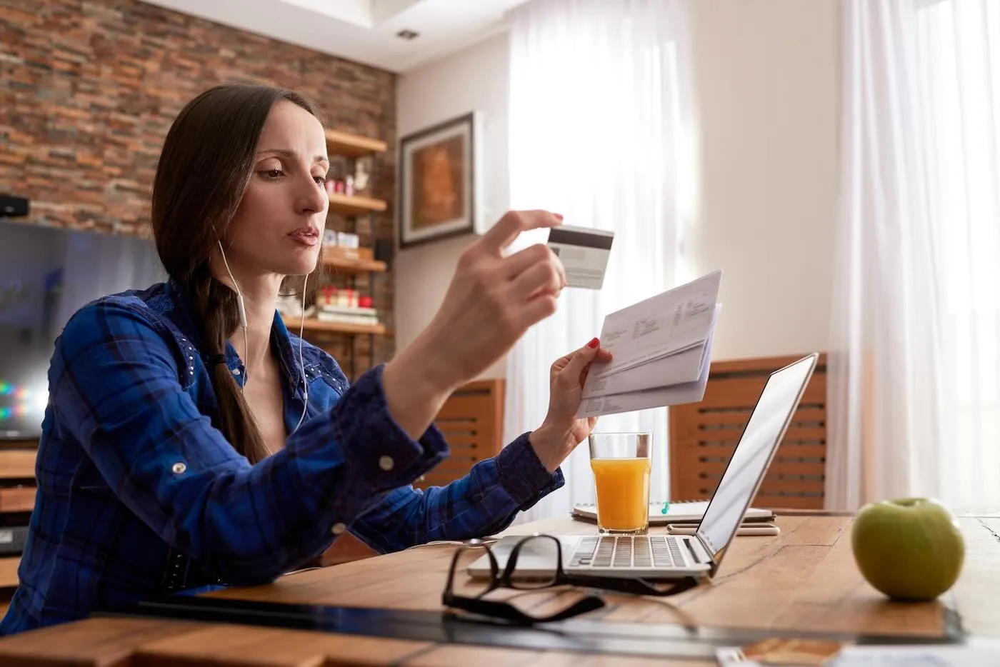 Woman is holding credit card and some letters while working on her laptop