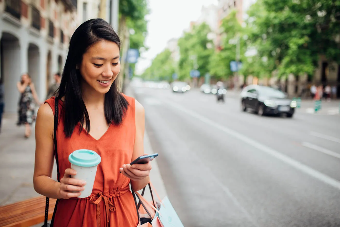 Woman walking on a sidewalk holding a coffee and her phone.