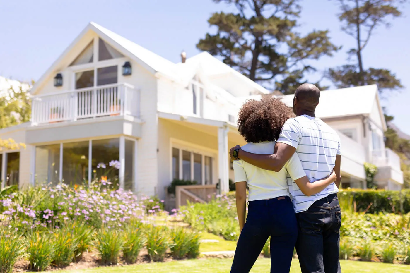 Couple embracing each other as they look at their new house outside from their front lawn.