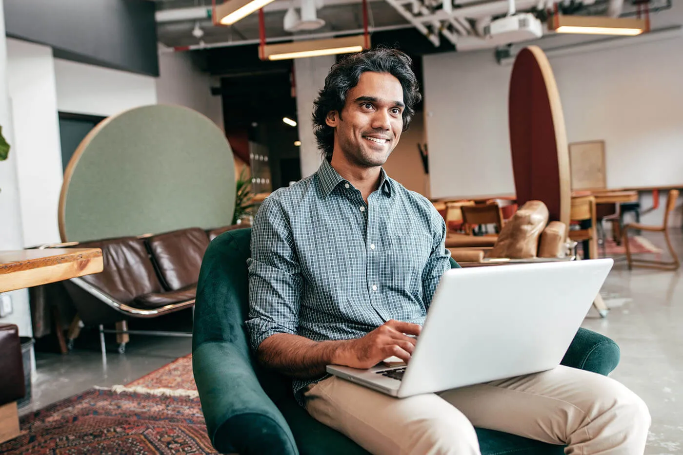 A man smiles while having his laptop on his lap as he sits down.