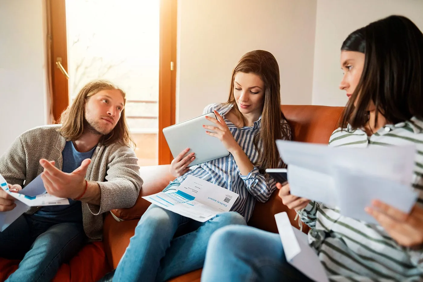 A group of three young people sit down and look at each other while holding documents.