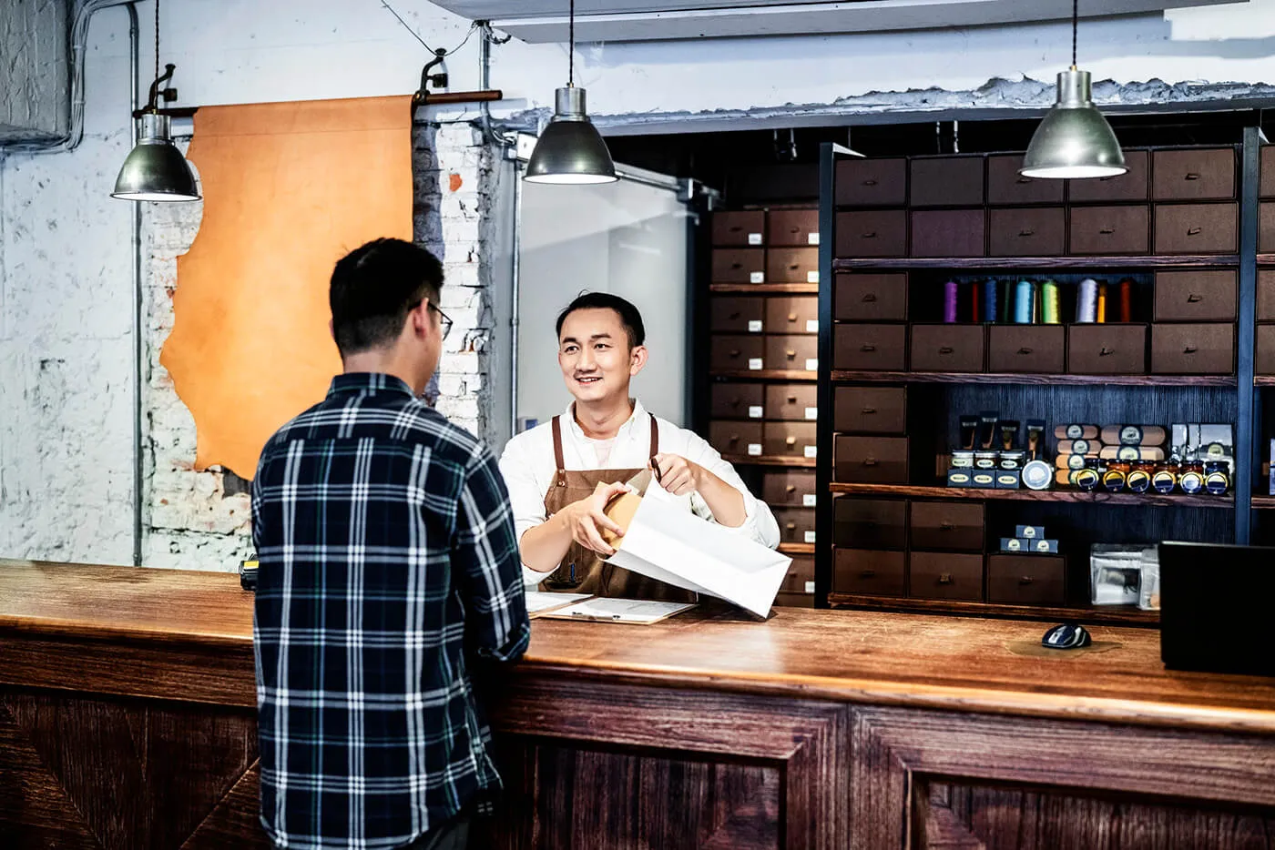 Store cleck packing a box while talking to customer at a checkout counter.