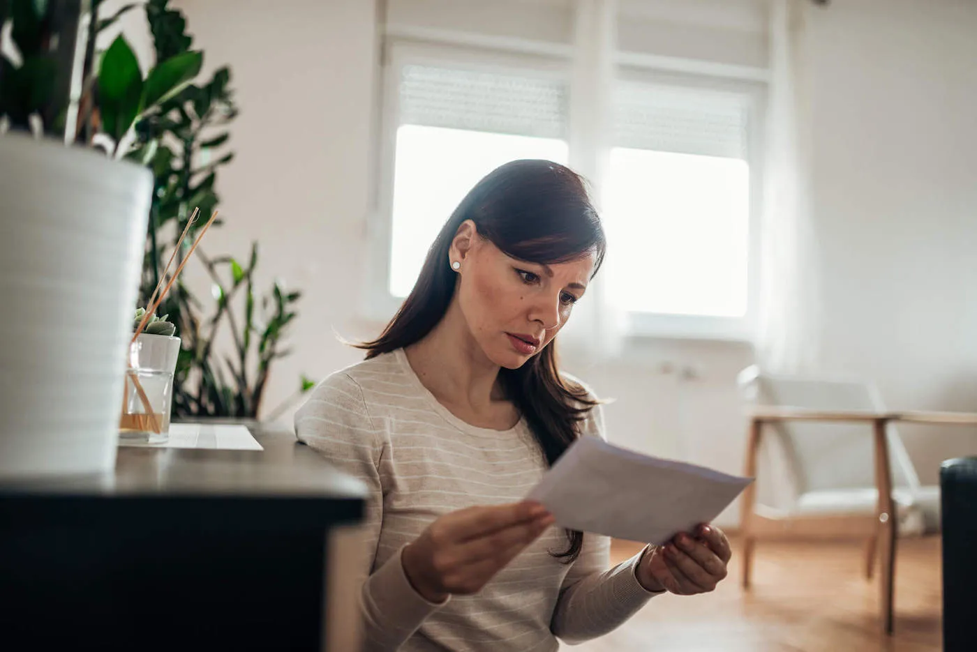 A woman frowns while holding a document at home.