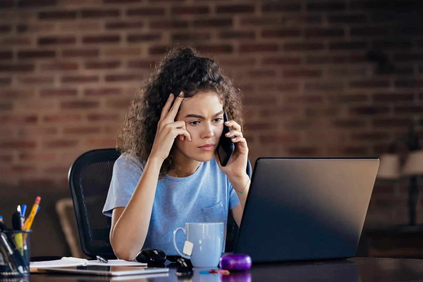 A woman on the phone frowns as she looks at her laptop computer.