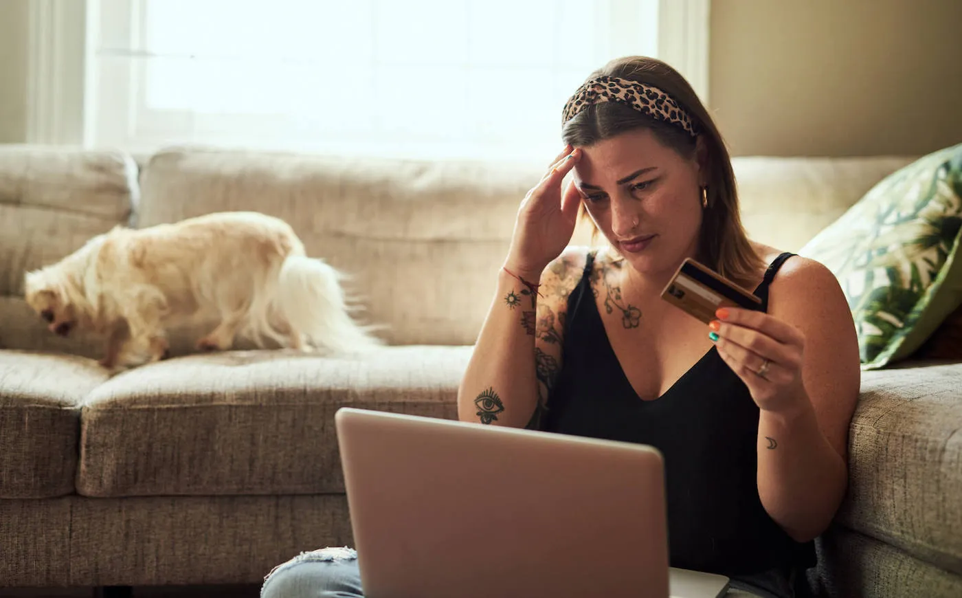 A woman holds her head while looking at her laptop and holding her credit card.