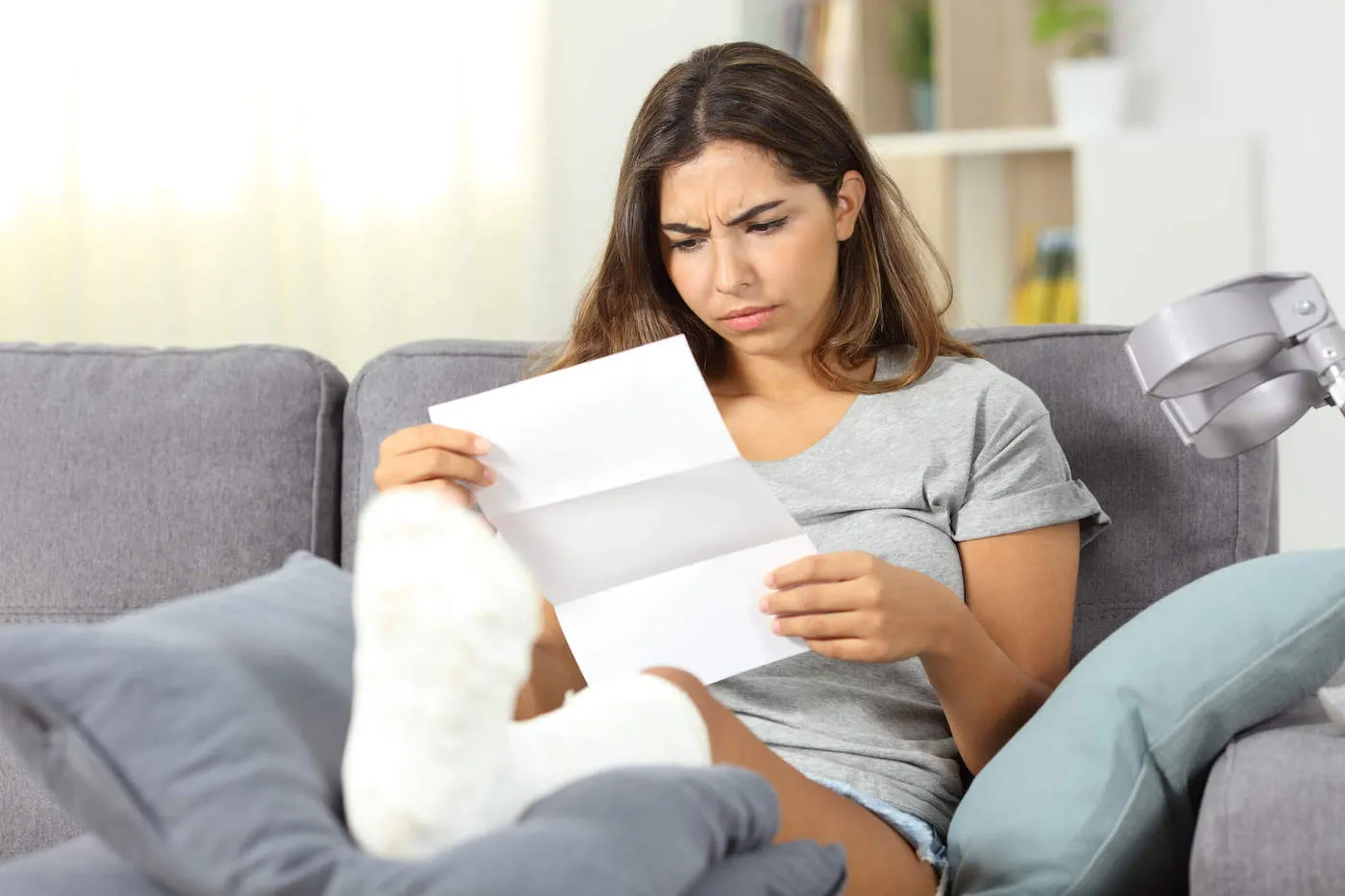 A woman looks at a document while her foot is in a cast under some pillows.