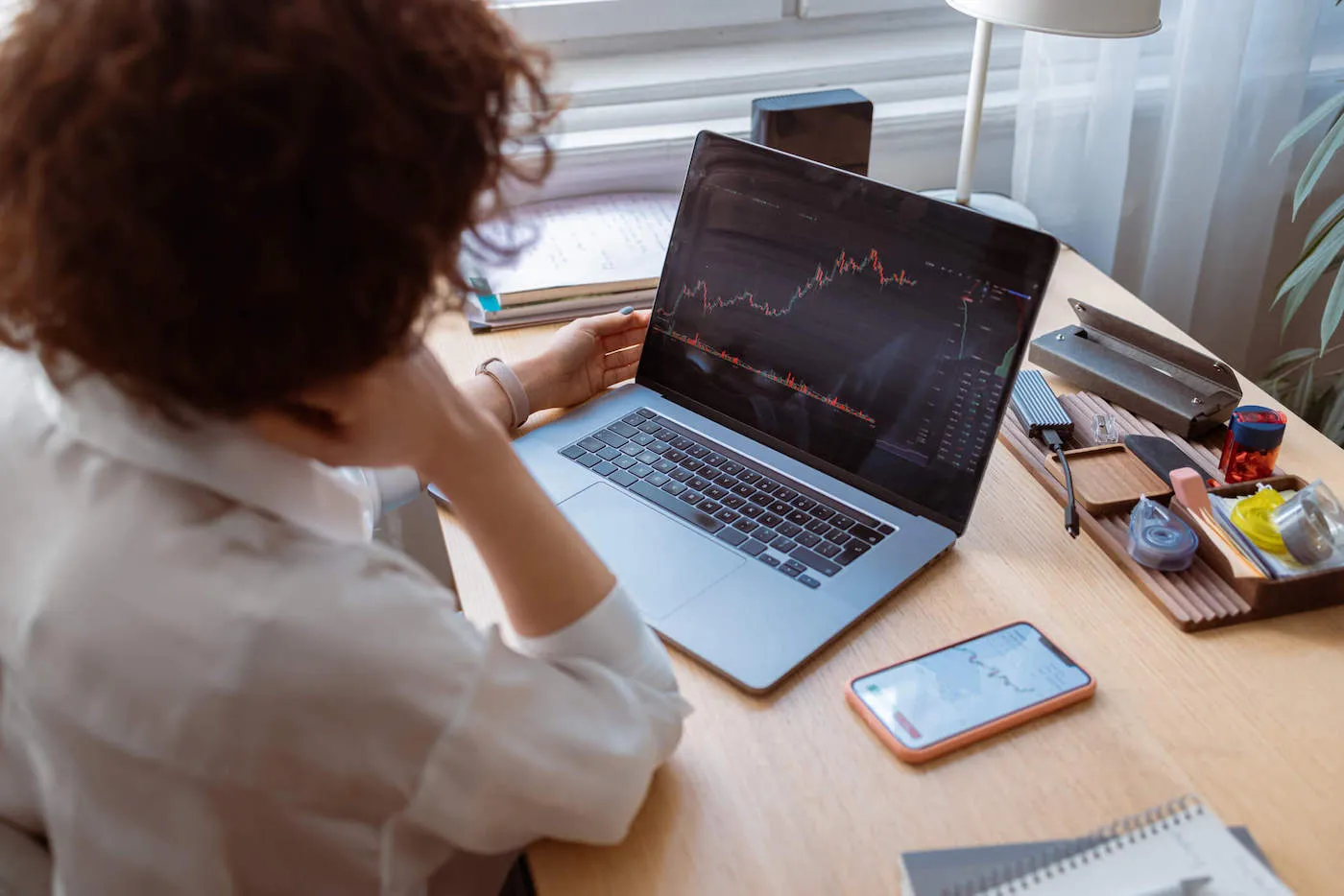 A woman wearing a white shirt looks at a stock chart on her laptop computer screen.