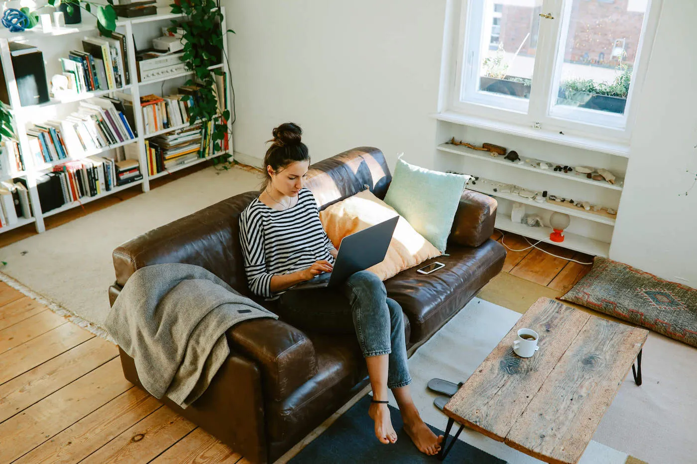 A woman wearing a striped shirt sits on the couch while she uses her laptop computer.