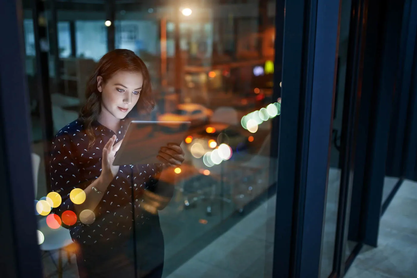 A woman wearing a black shirt uses a tablet while next to the window in her office.