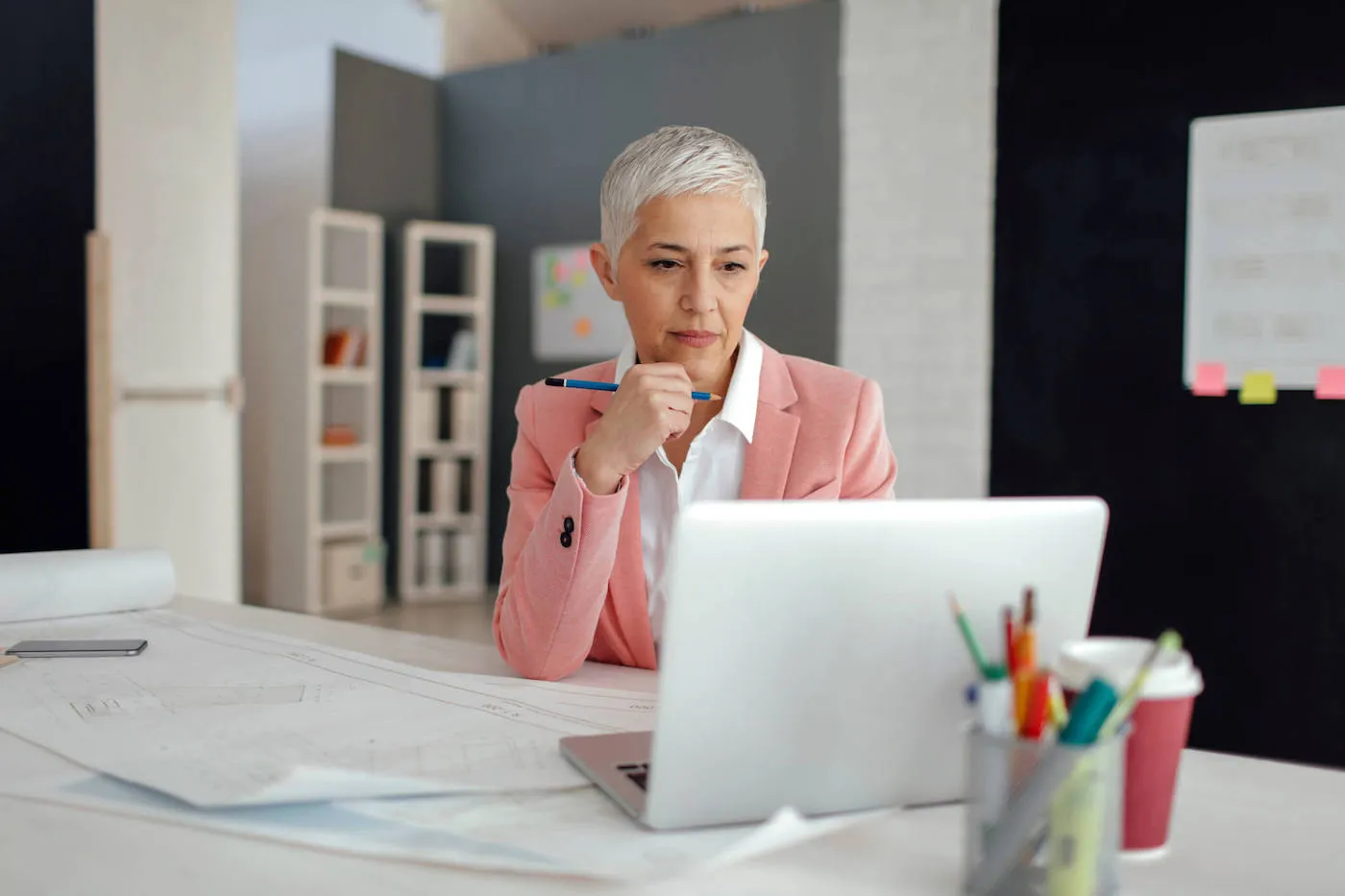 Woman wearing a pink suit is looking at her laptop screen at her office.