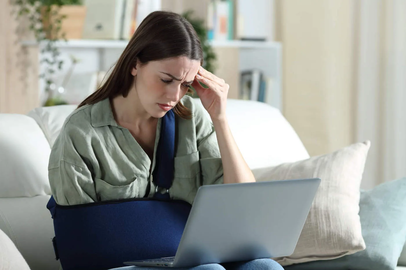 A woman wearing an arm cast looks at a laptop computer while placing her fingers to her head.