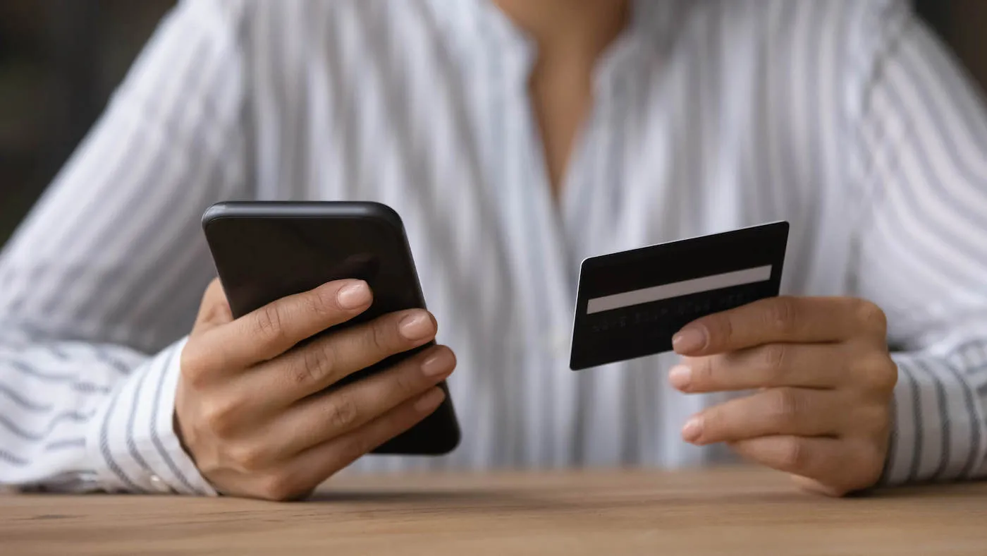 Woman in white shirt holding checking credit card info on mobile phone.