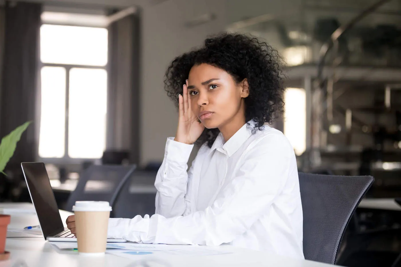 A young lady frowns and looks out the window while at work.