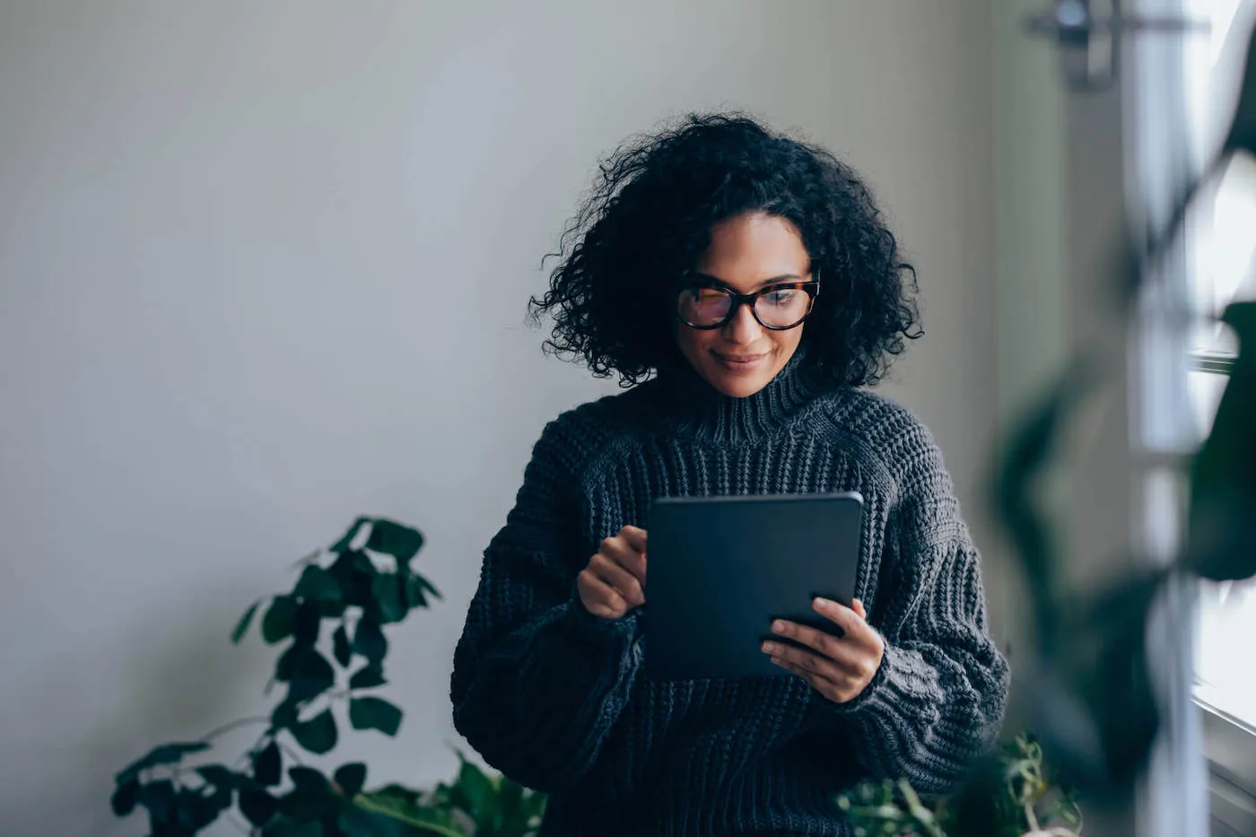 Young business woman with eyeglasses working on her digital tablet while standing in the living room.