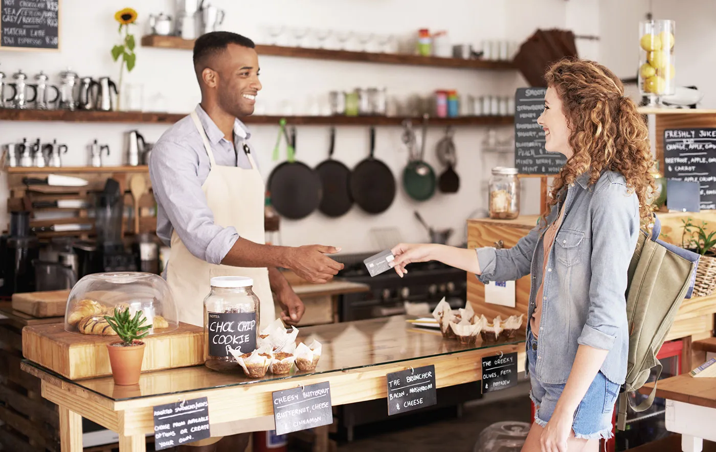 A customer hands over their credit card to a store owner wearing an apron.